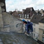 Technicien 2NM Propreté nettoyant un mur en pierre tagué à la nacelle