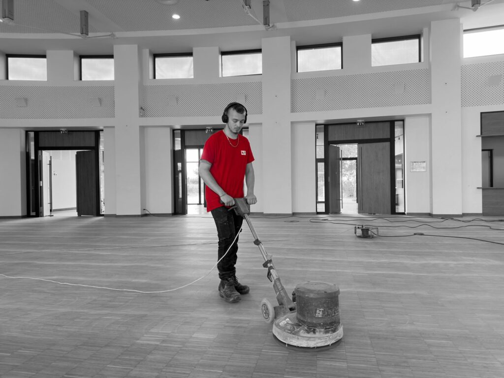 Agent polyvalent en train de rénover un parquet dans une salle de réception
